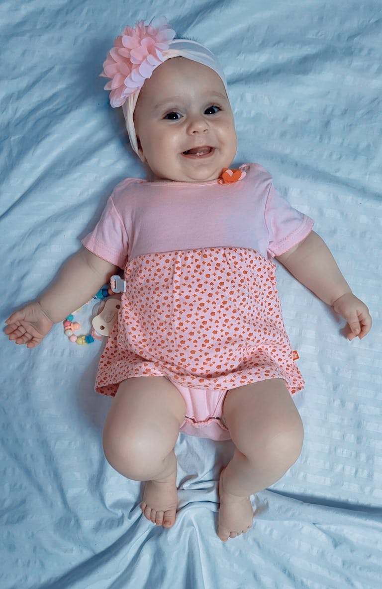Adorable baby girl in a pink outfit lying on a blue blanket, smiling happily.